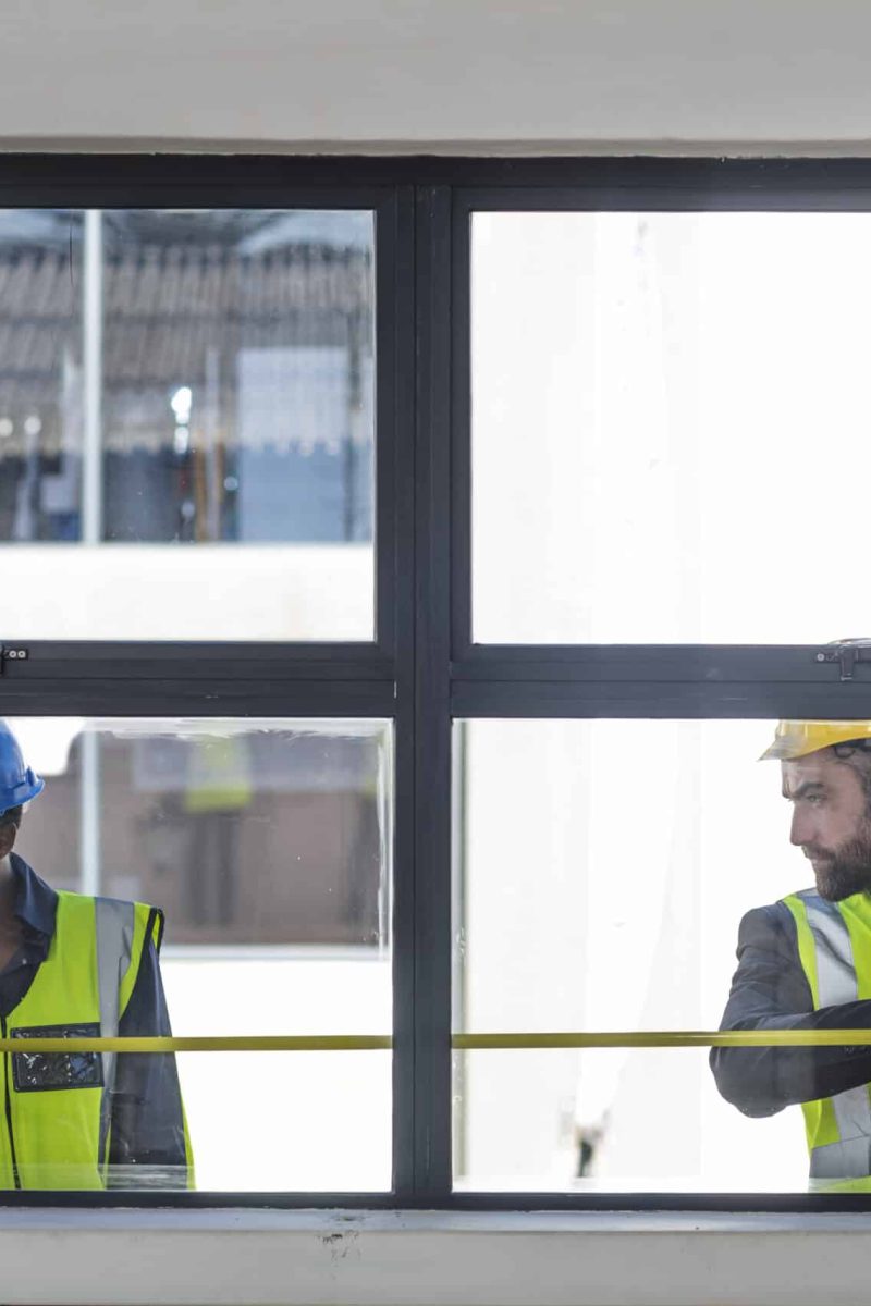 Colleagues in hard hats and high viz jackets measuring window Colleagues in hard hats and high viz jackets measuring window