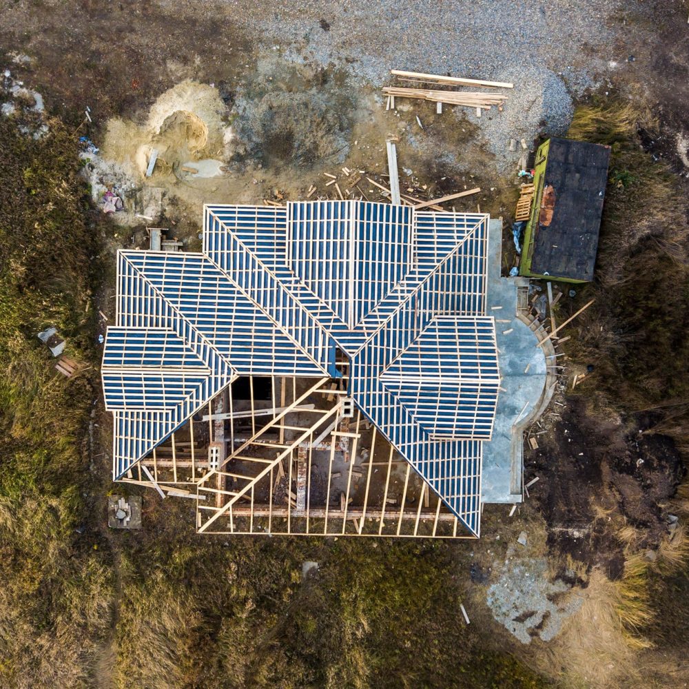Private residential house with wooden roof frame structure under construction. Unfinished brick building under development.