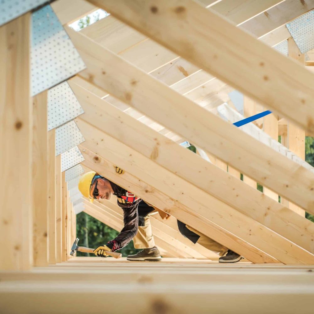Wooden Home Frame Construction. Caucasian Contractor in His 30s Wearing Hard Hat. Residential Construction.